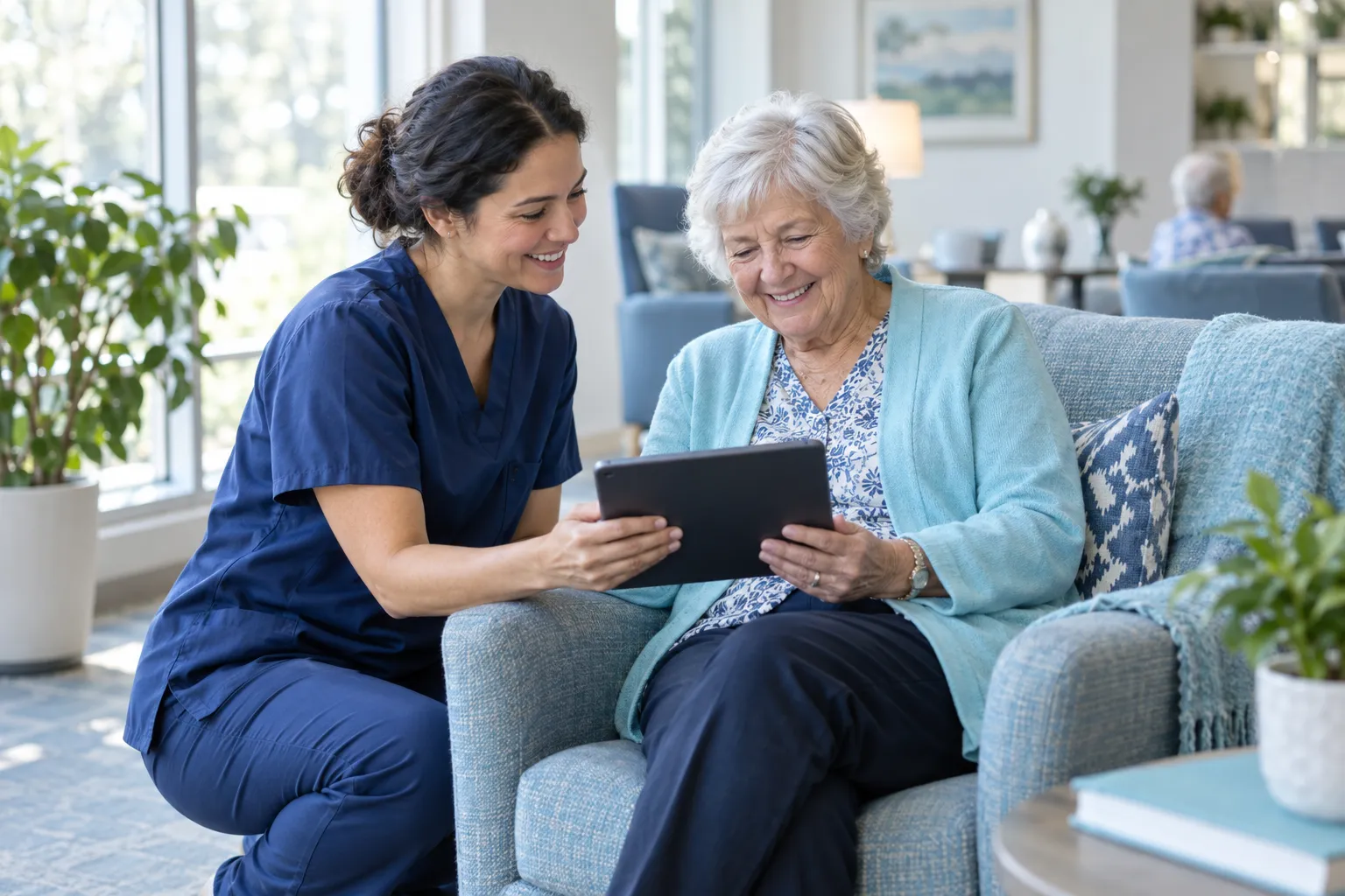 A nurse and an older resident share a laugh while reviewing a tablet together.